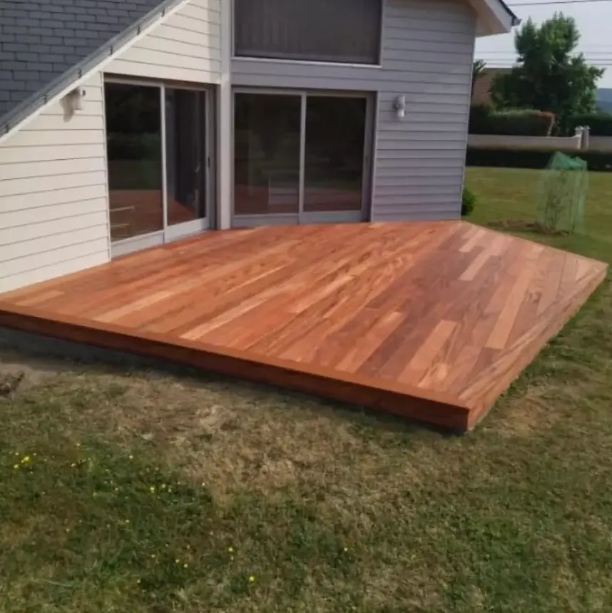 Terrasse en bois neuve attenante à une maison moderne avec bardage clair et grandes baies vitrées, sur un jardin verdoyant