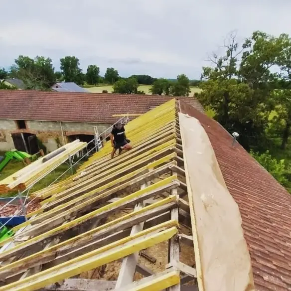 Rénovation de toiture sur un bâtiment ancien, avec un ouvrier installant une nouvelle structure en bois sur la charpente, entouré d’échafaudages et d’outils