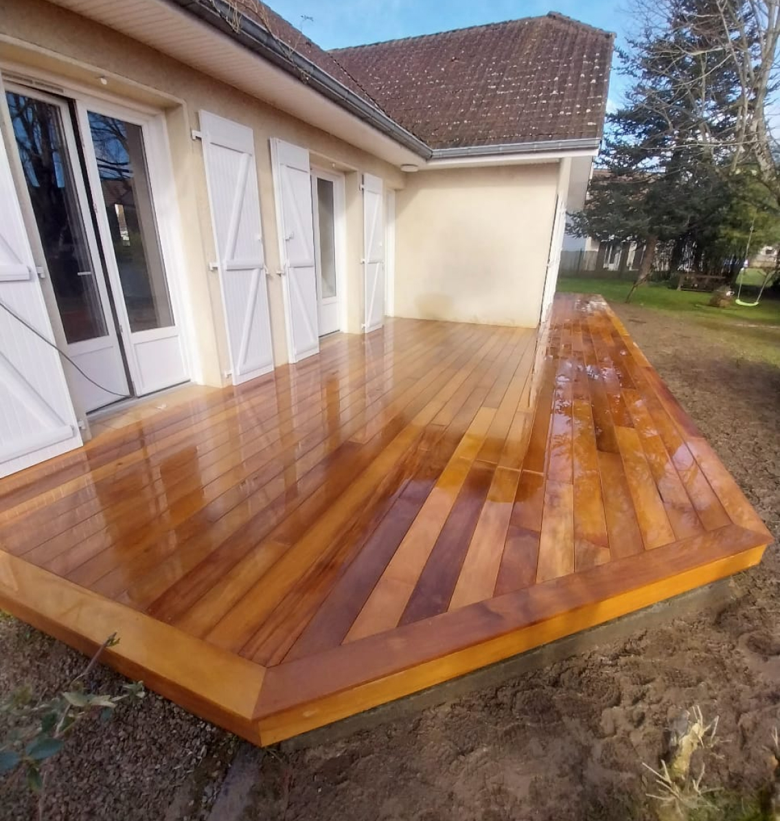 Terrasse en bois fraîchement installée devant une maison avec volets blancs, offrant un aménagement extérieur élégant et naturel.