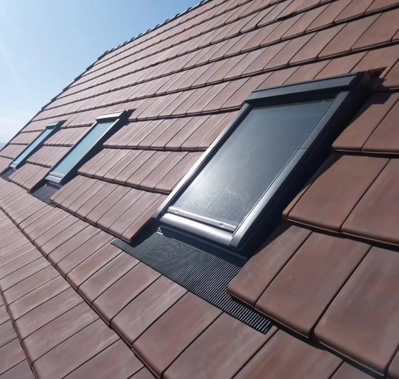 Toiture rénovée avec des tuiles en terre cuite et trois fenêtres de toit Velux assurant luminosité et ventilation sous un ciel ensoleillé.