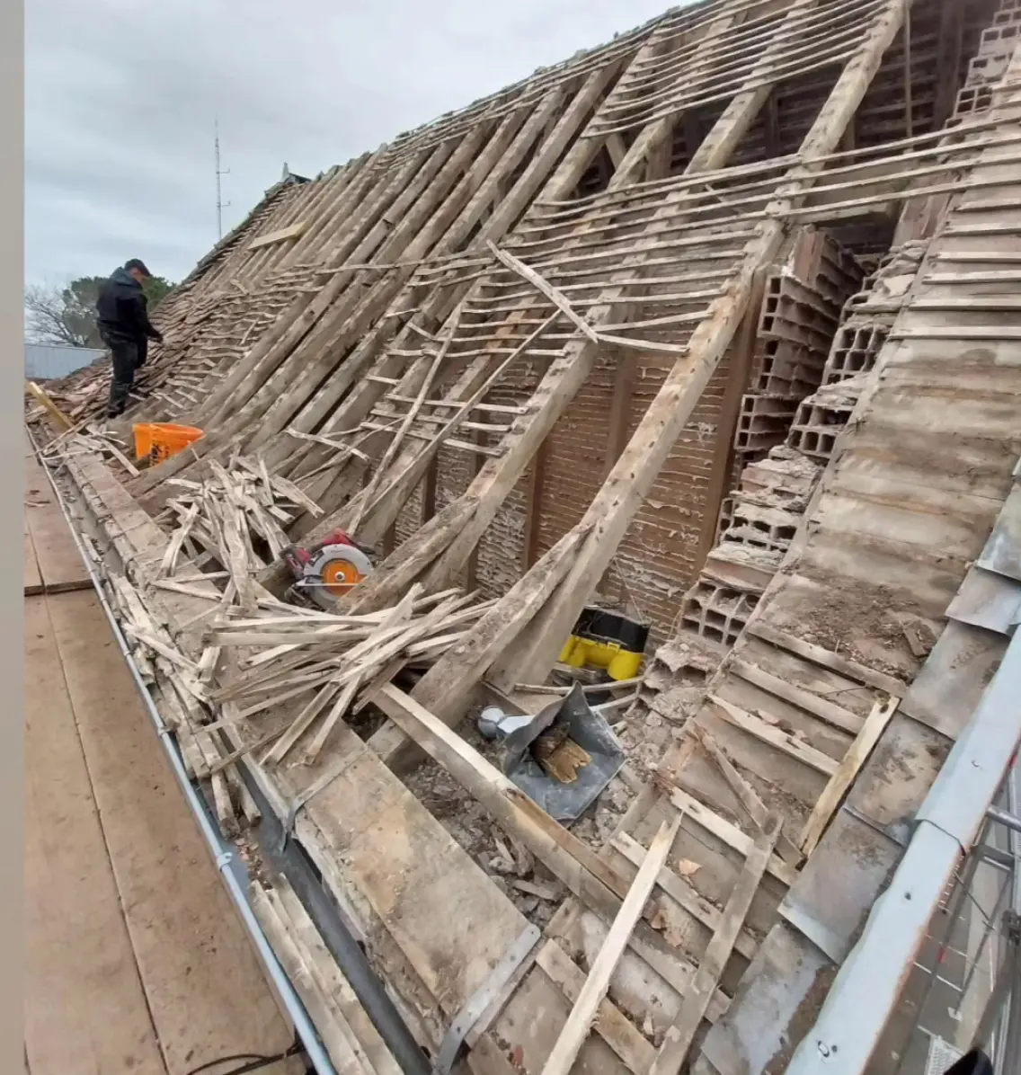 Travaux de rénovation de toiture avec la dépose de l'ancienne charpente en bois et des tuiles, exposant la structure du toit avant la reconstruction.