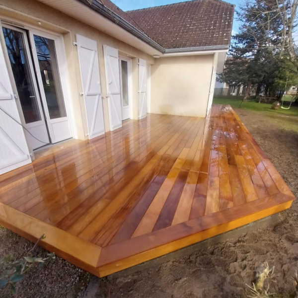 Terrasse en bois fraîchement installée devant une maison avec volets blancs, offrant un aménagement extérieur élégant et naturel.