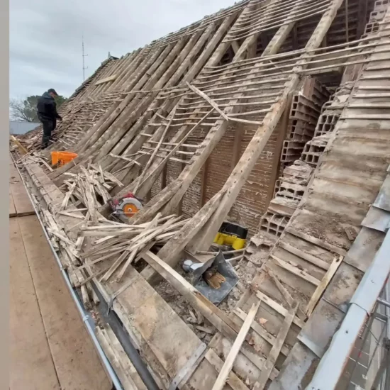Travaux de rénovation de toiture avec la dépose de l'ancienne charpente en bois et des tuiles, exposant la structure du toit avant la reconstruction.